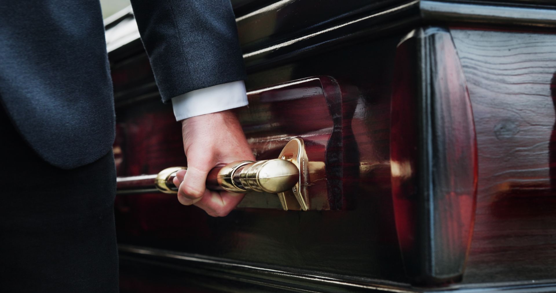 Person in a suit placing a brass handle on a dark coffin-like box with red wood accents