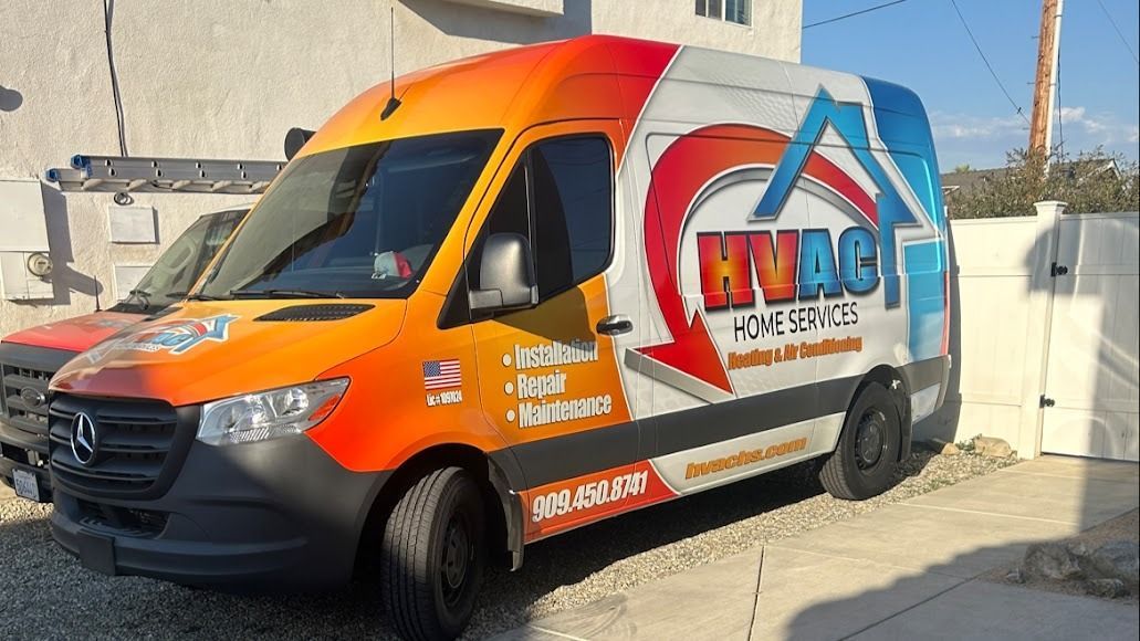 Orange and white service van with company logo parked beside a white wall in bright sunlight