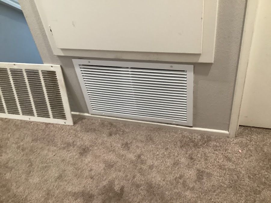 White wall vents along a beige carpeted hallway beside a closed door