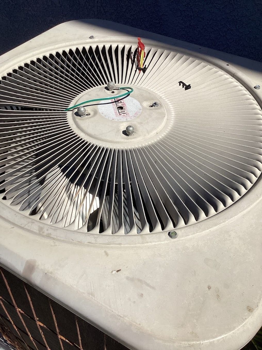 Top view of a round air conditioner condenser fan with exposed wiring and a dirty outer casing.