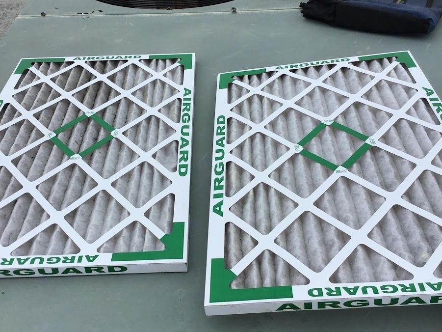 Two white air filters in green frames lying side by side on a gray surface.
