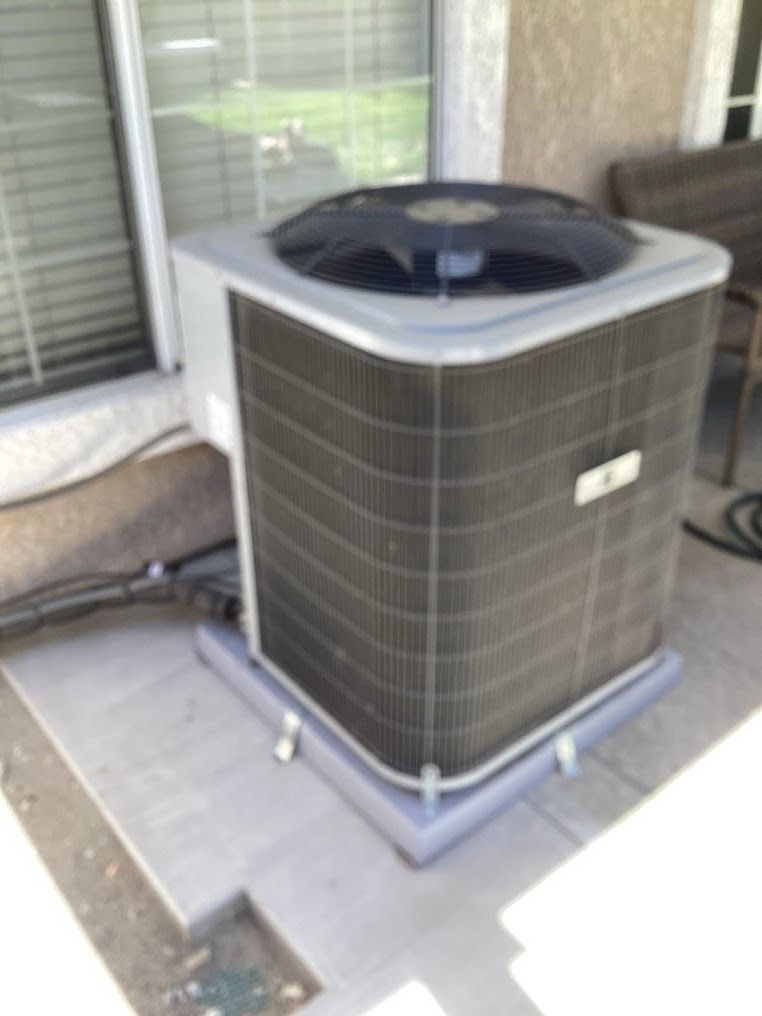Outdoor HVAC air conditioner unit on a patio beside a sliding glass door.
