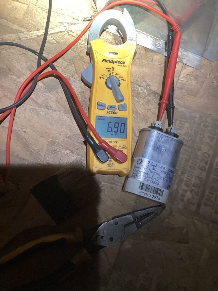 Multimeter testing a silver capacitor on a wooden surface with red and black leads attached
