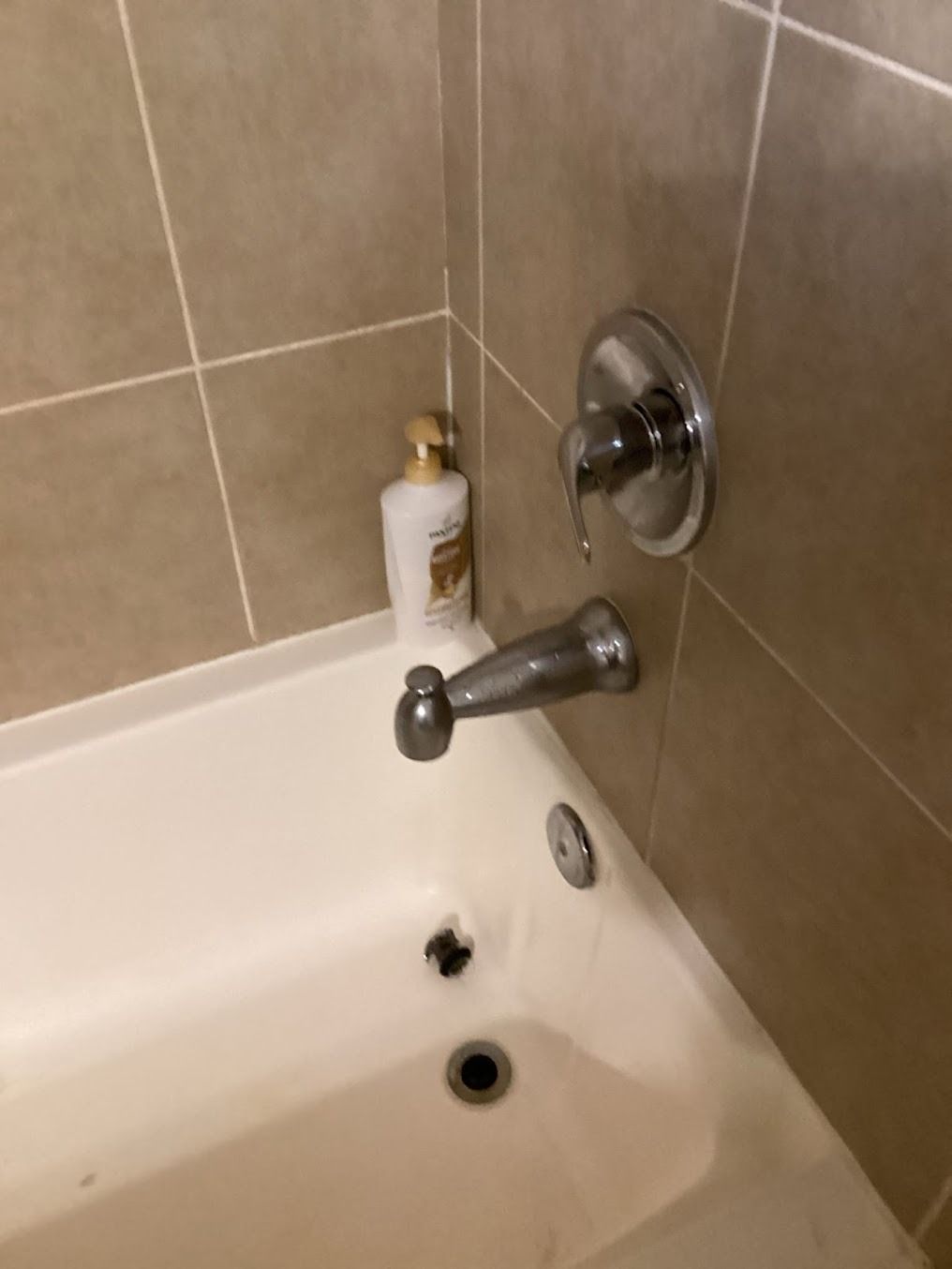 Bathroom sink with chrome faucet, soap dispenser, and beige tiled wall.