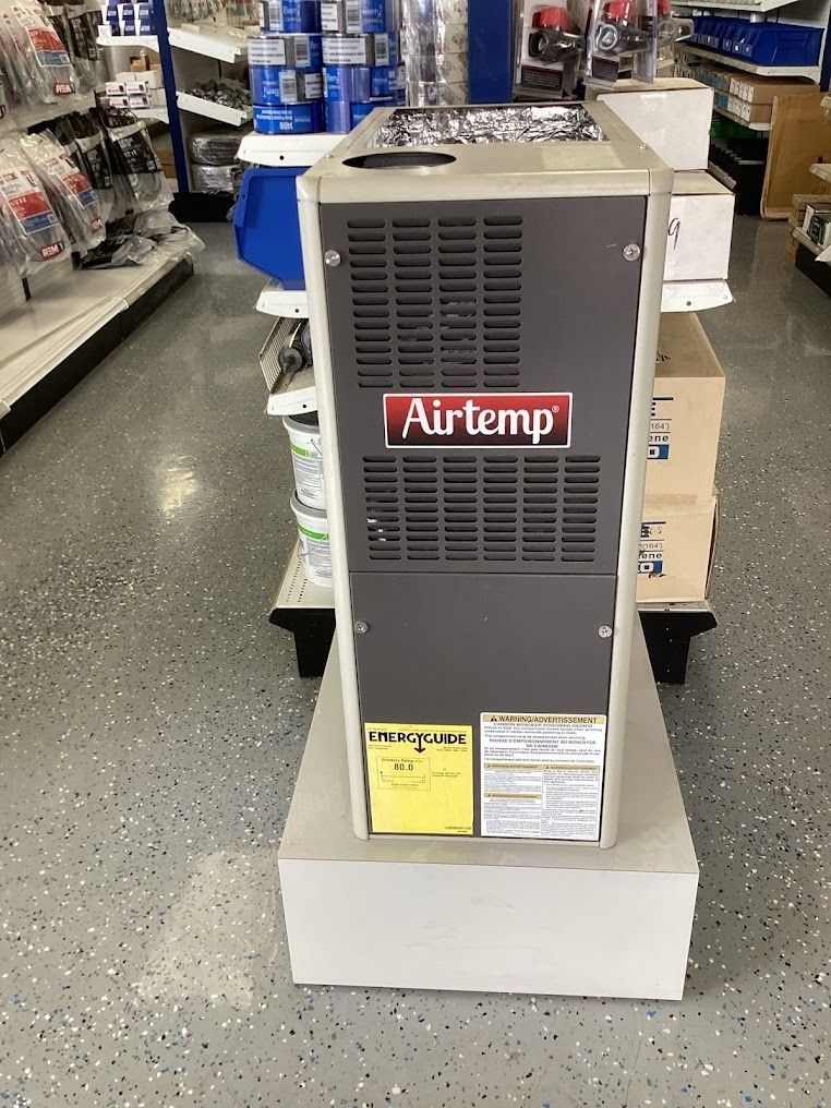 Gray Airtemp appliance on a store display stand in an aisle, with product labels and shelving in the background
