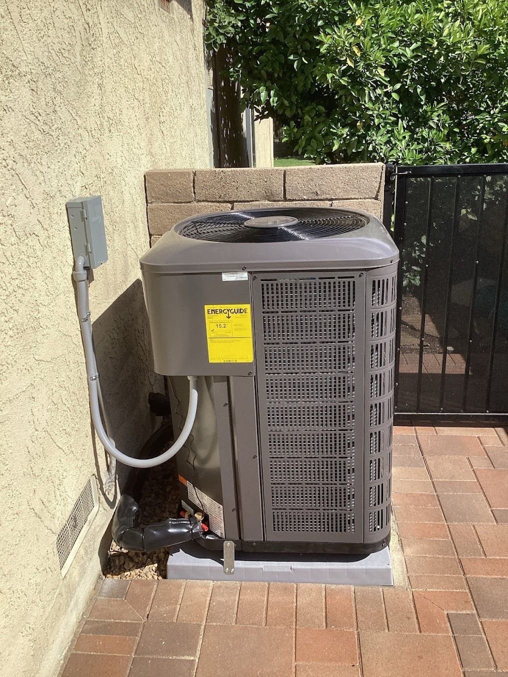 Outdoor HVAC unit beside a stucco wall and black gate on a brick patio