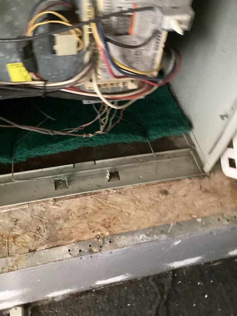 Open furnace cabinet with exposed wiring and metal components above a dusty floor opening