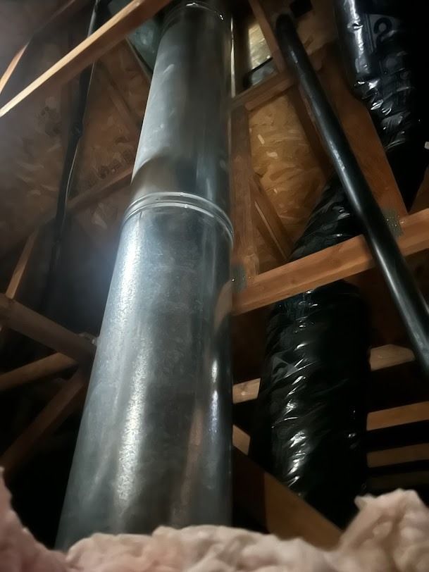 Metal HVAC ductwork in an attic with wooden beams and insulation