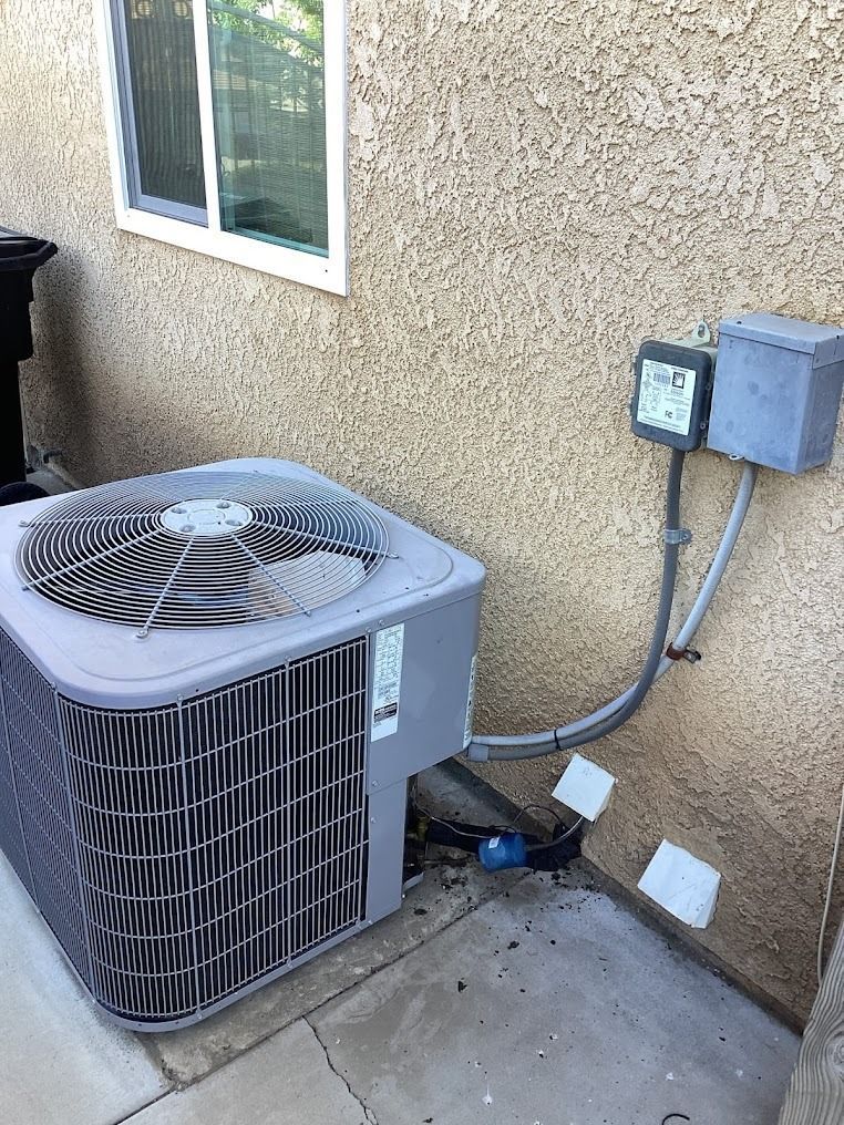 Outdoor air conditioner unit beside a stucco wall with electrical boxes and conduit
