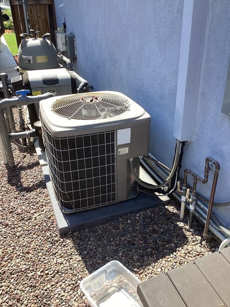 Outdoor air conditioner unit beside a stucco wall, with piping and another unit in the background.