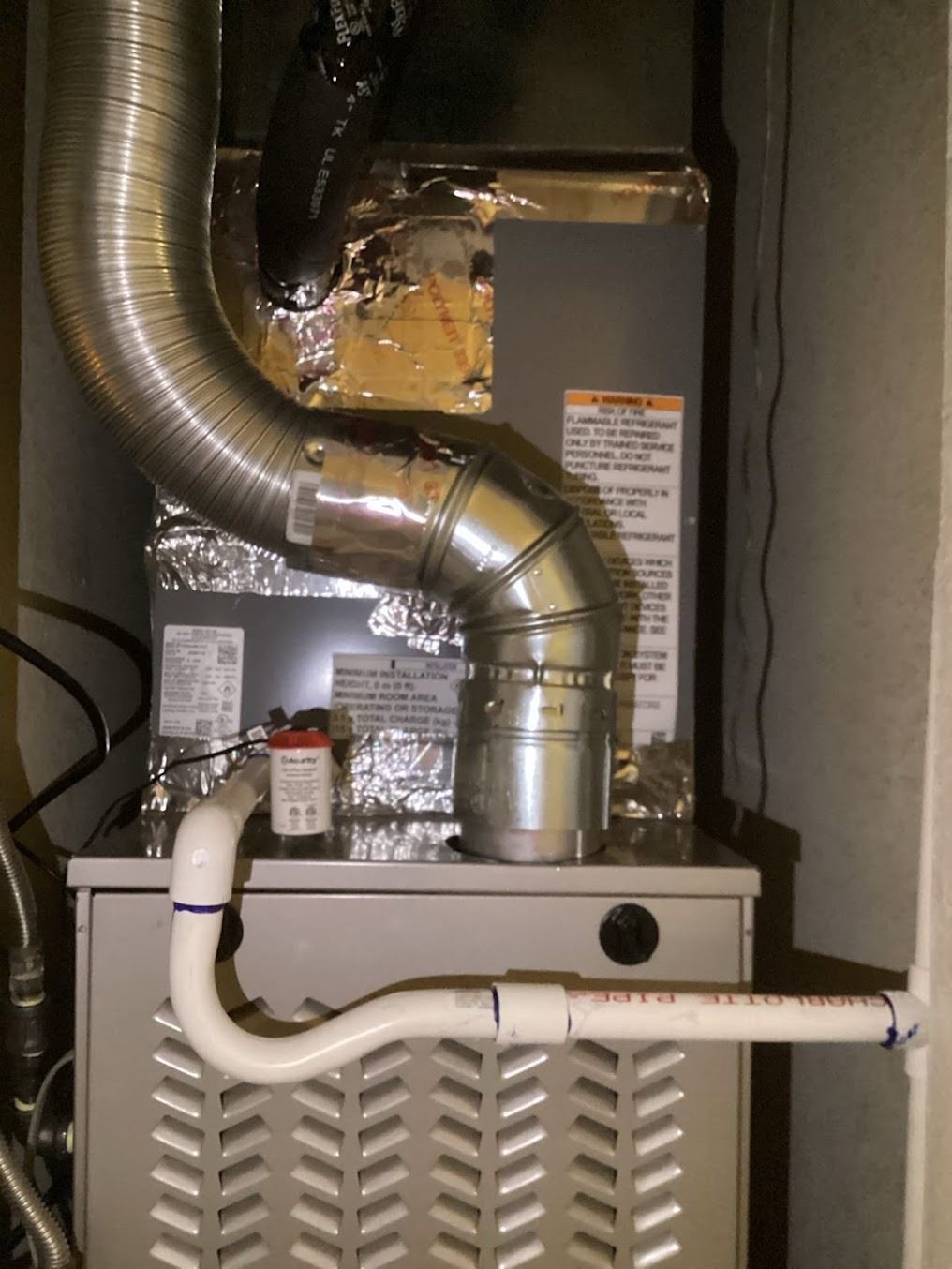 Furnace with silver ductwork and white PVC pipes in a utility closet