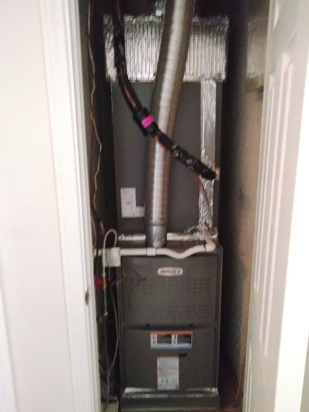 Utility furnace in a narrow closet, with exposed ductwork, pipes, and wiring.