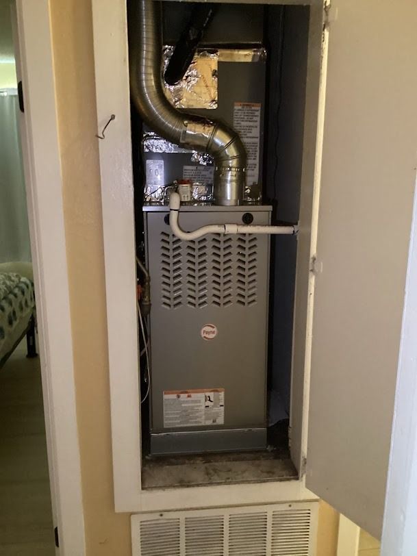 Open furnace in a closet with exposed ductwork and pipes