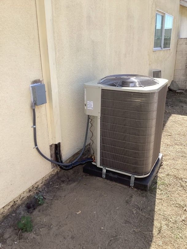 Outdoor HVAC unit beside a beige house wall, with electrical conduit and a window nearby.