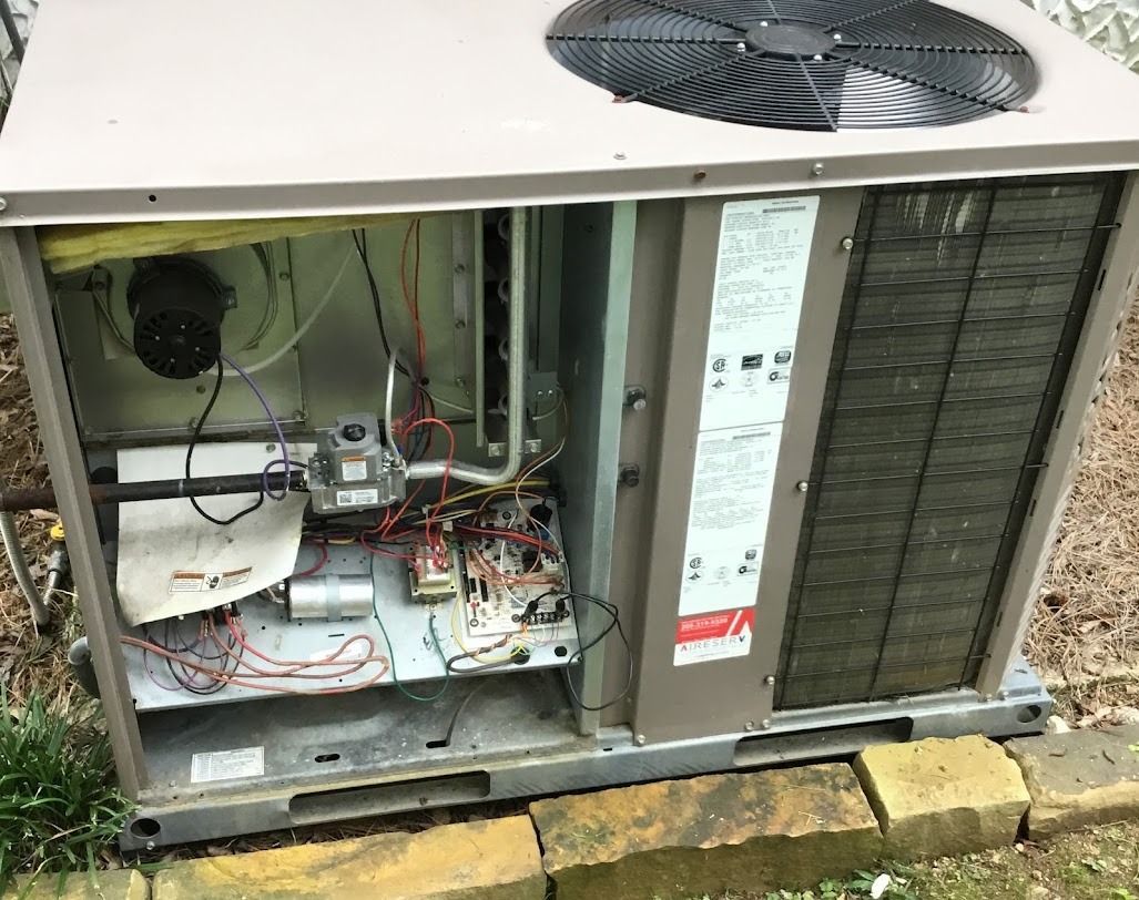 Open HVAC unit with exposed wiring and components beside a grassy outdoor area.