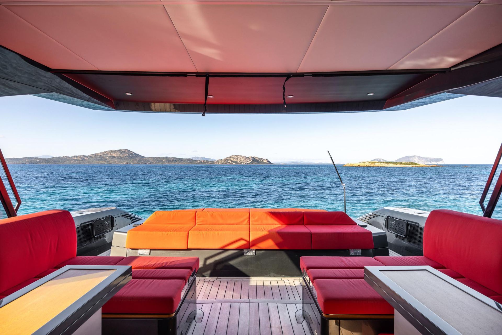 The inside of a boat with red seats and tables overlooking the ocean.