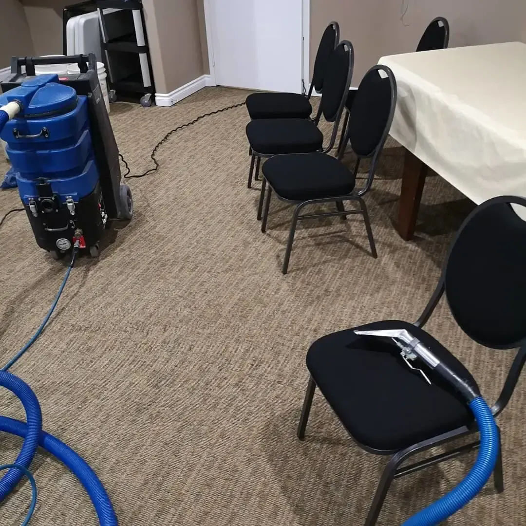 Meeting room with black chairs, carpet, blue cleaning equipment, and a table covered with a white cloth.