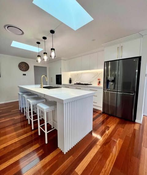 A Kitchen With a Large Island and Stools and a Stainless Steel Refrigerator — Darko's Kitchens in Shoalhaven, NSW