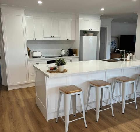 A Kitchen With White Cabinets , a Large Island , Stools and a Refrigerator — Darko's Kitchens in Shoalhaven, NSW