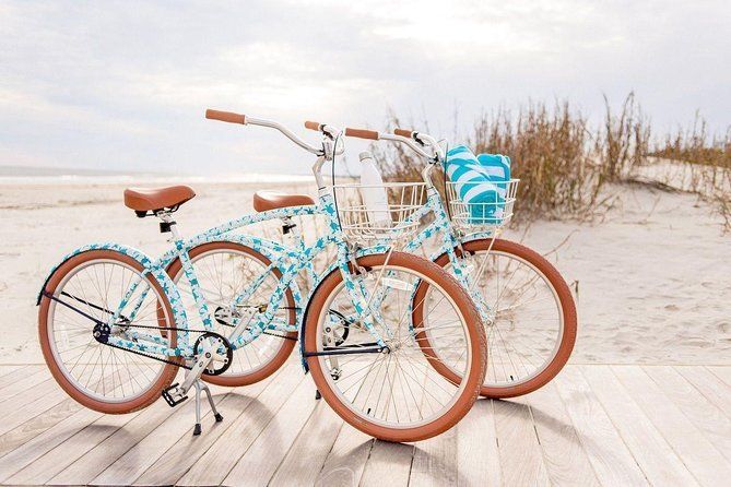 Two light blue cruiser bicycles with brown seats and tires on a boardwalk overlooking a beach.