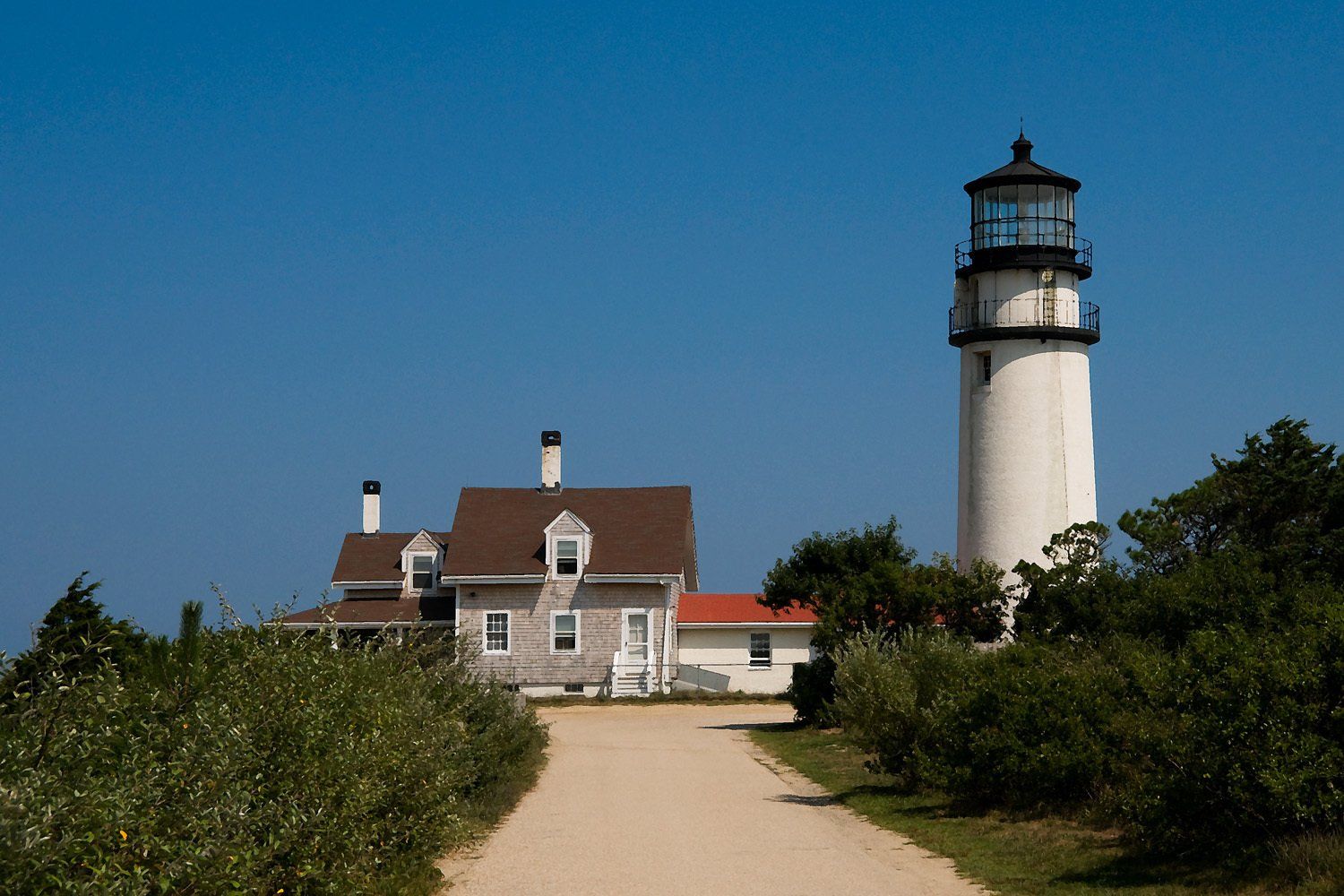 White lighthouse and attached house on a sunny day with a clear blue sky.