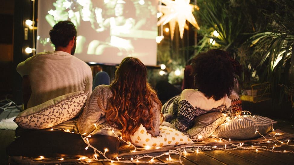 People watching a movie outdoors on cushions, under string lights and a star.