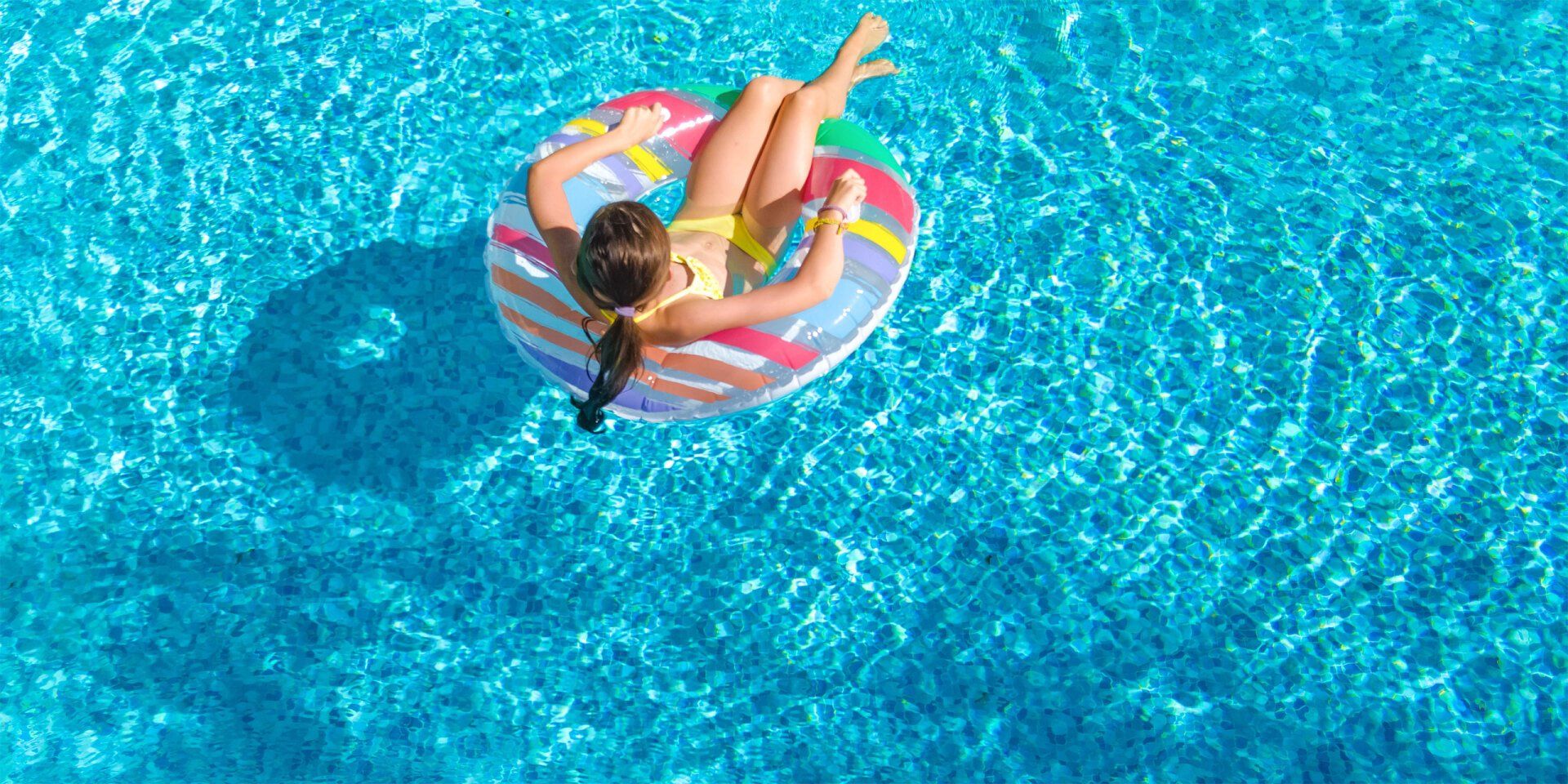 A person floats on an inflatable ring in a blue swimming pool on a sunny day.