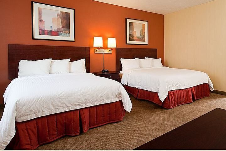 Hotel room with two queen beds, red bed skirts, brown headboards, and orange and beige walls.