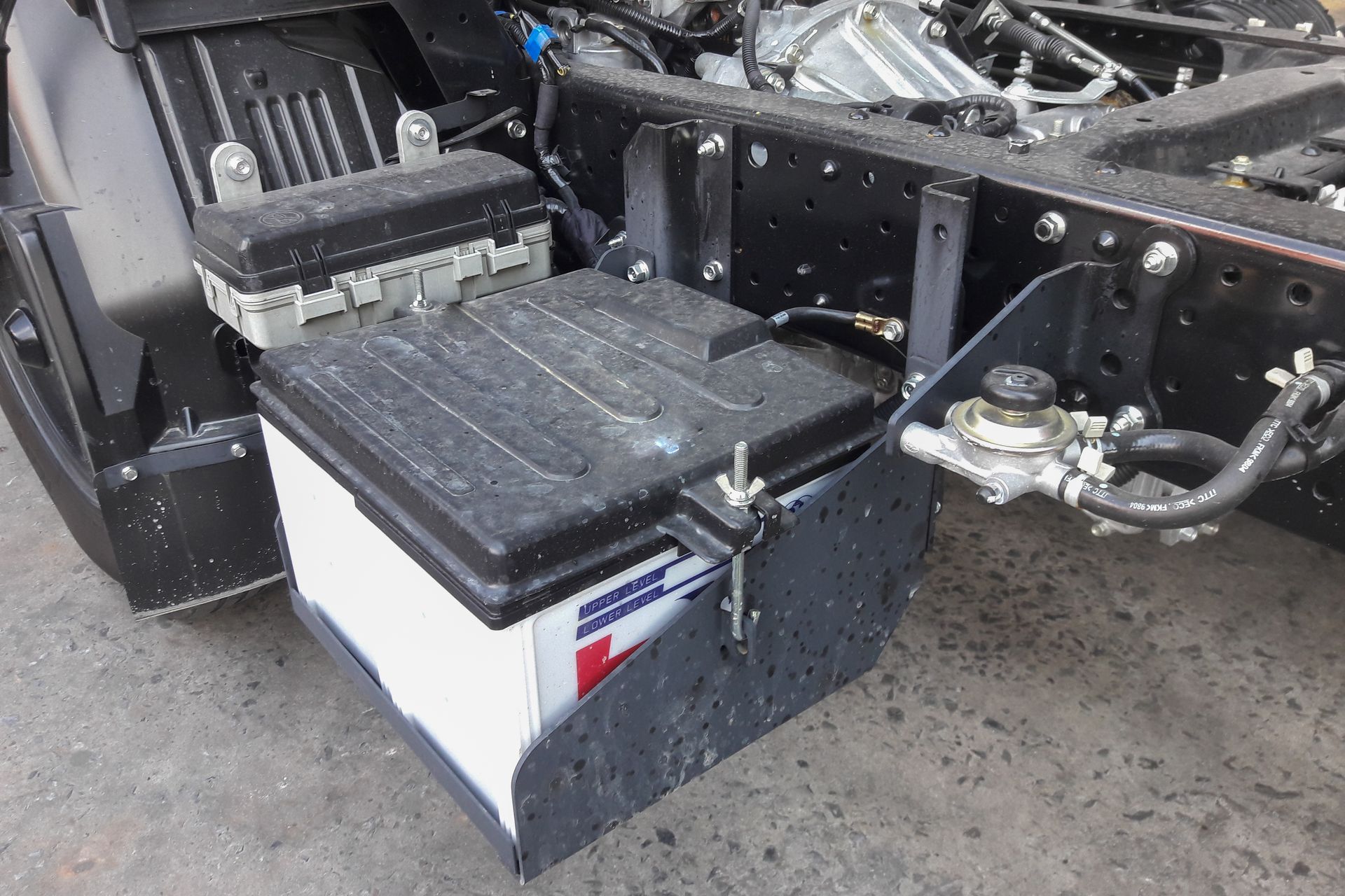 A person uses a T-handle wrench to tighten a terminal on a red car battery under the hood of a vehicle.