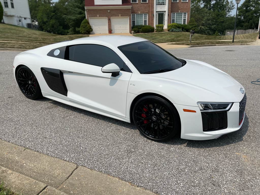 White Audi R8 sports car with black wheels parked on a gray asphalt driveway.