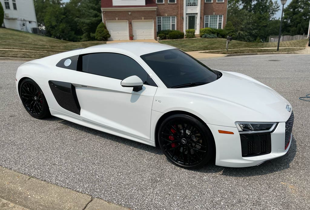 White Audi R8 sports car parked on a paved road. Black wheels, tinted windows, and red brake calipers visible.