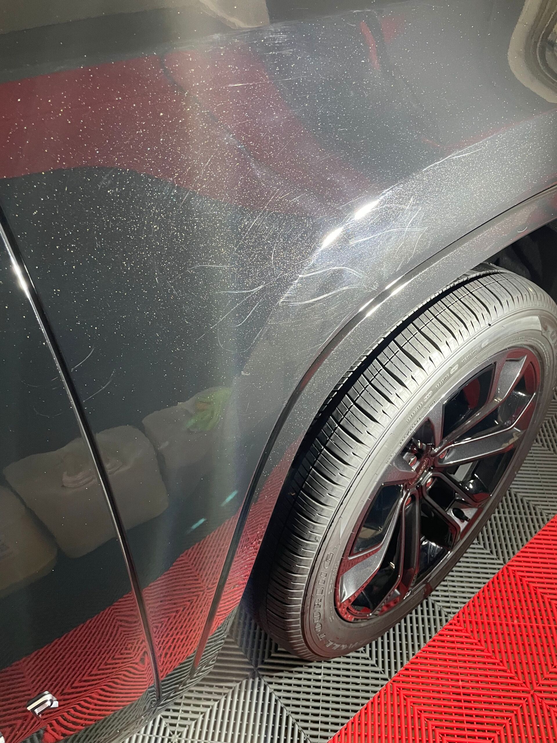 Dark gray car fender with wheel, showing metallic flecks, scratches, and black tire.