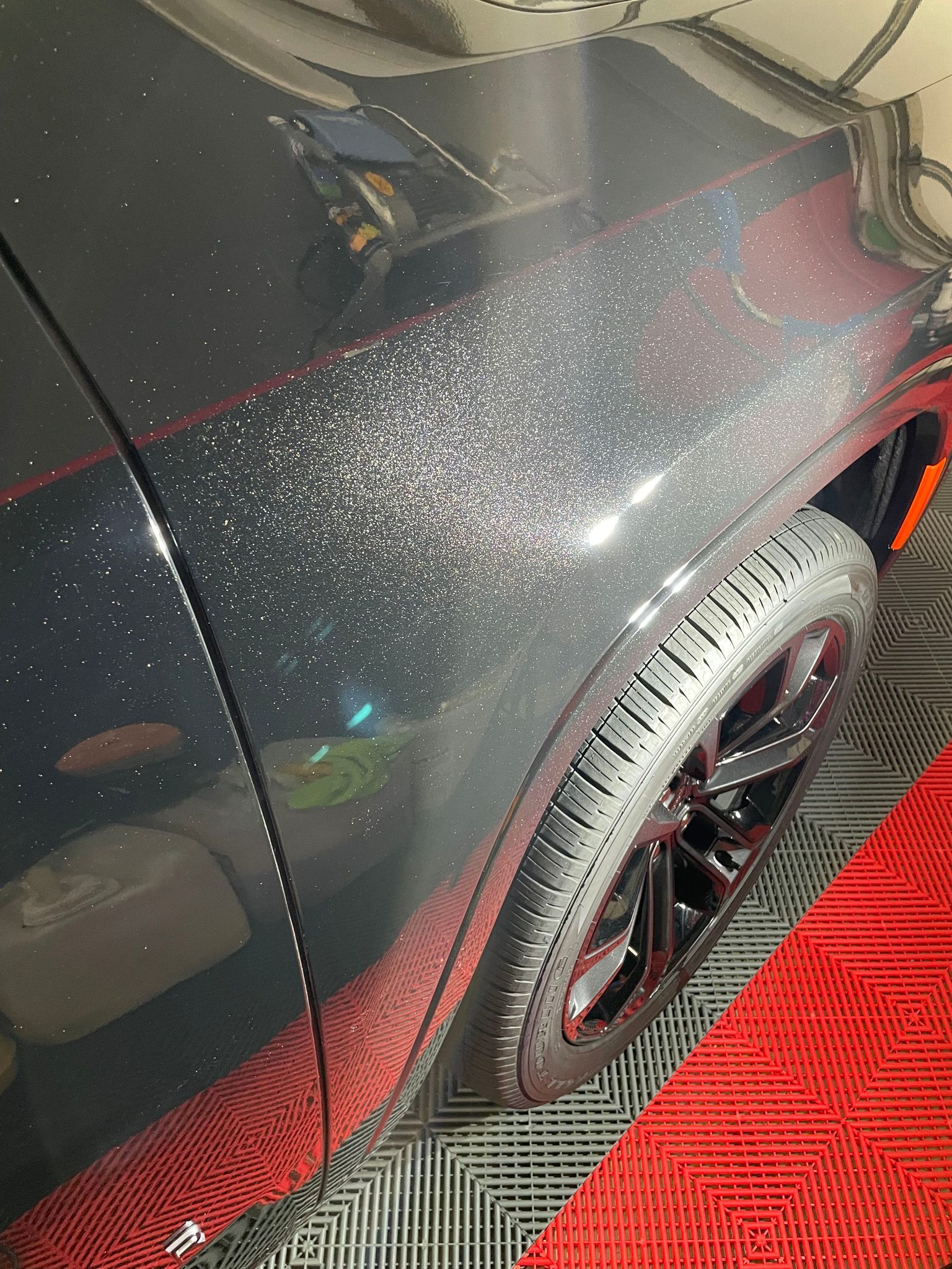 Black car fender with sparkling particles, black tire and rim on a red-tiled floor.