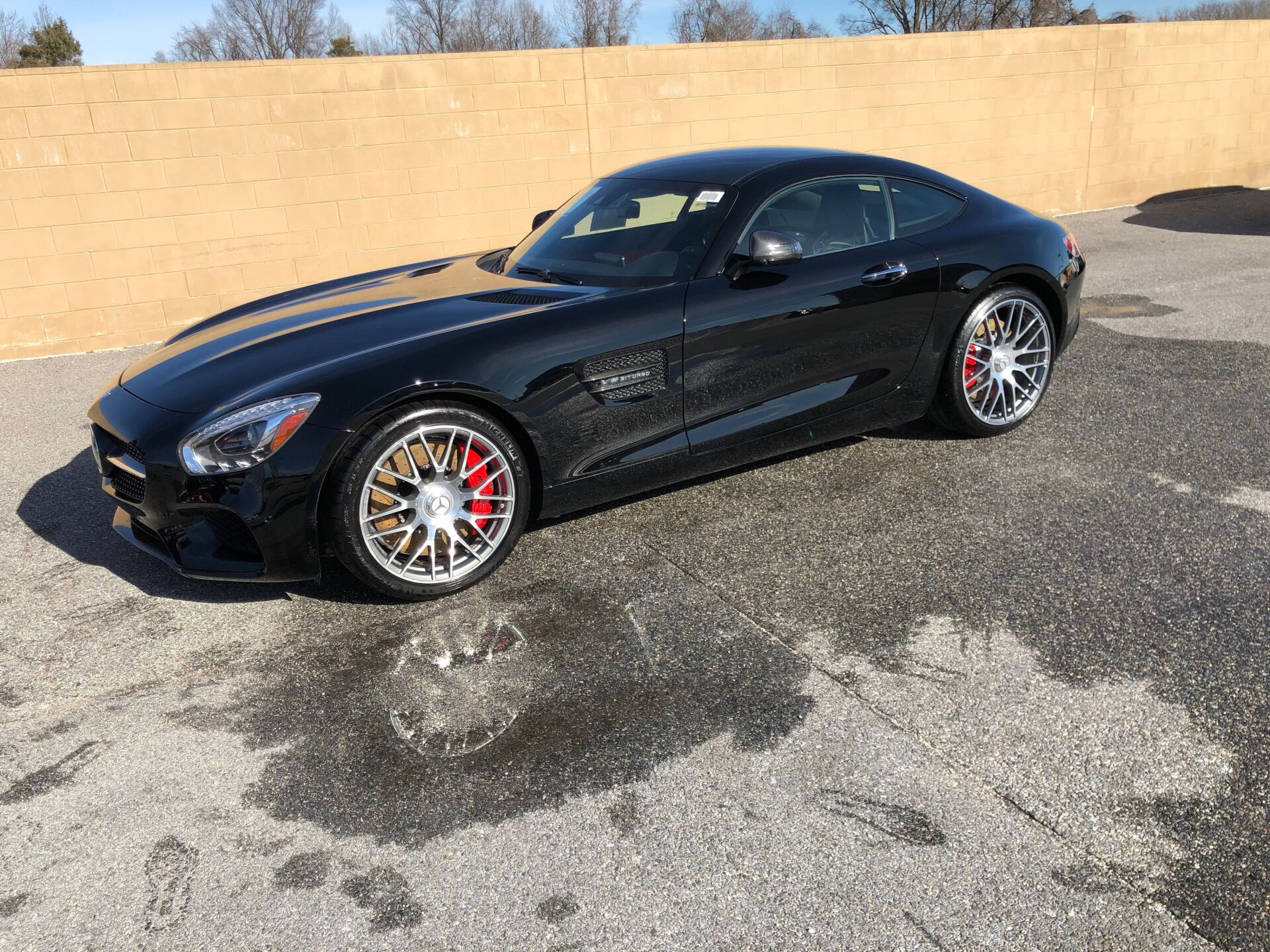 Black sports car parked on wet pavement with red brake calipers.