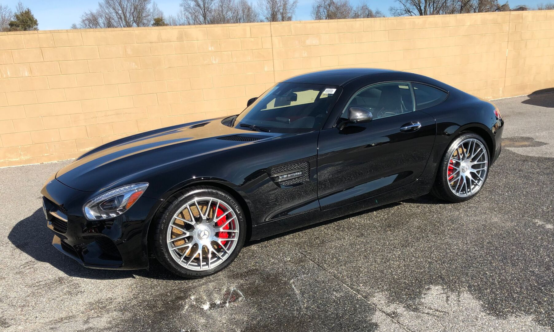 Black Mercedes-AMG GT coupe parked on a shiny surface in front of a beige wall, with red brake calipers and chrome wheels.
