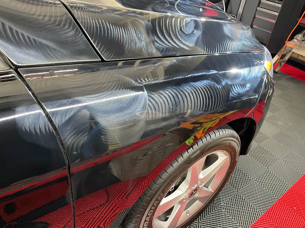 Black car body with swirling, reflective patterns, possibly from detailing.