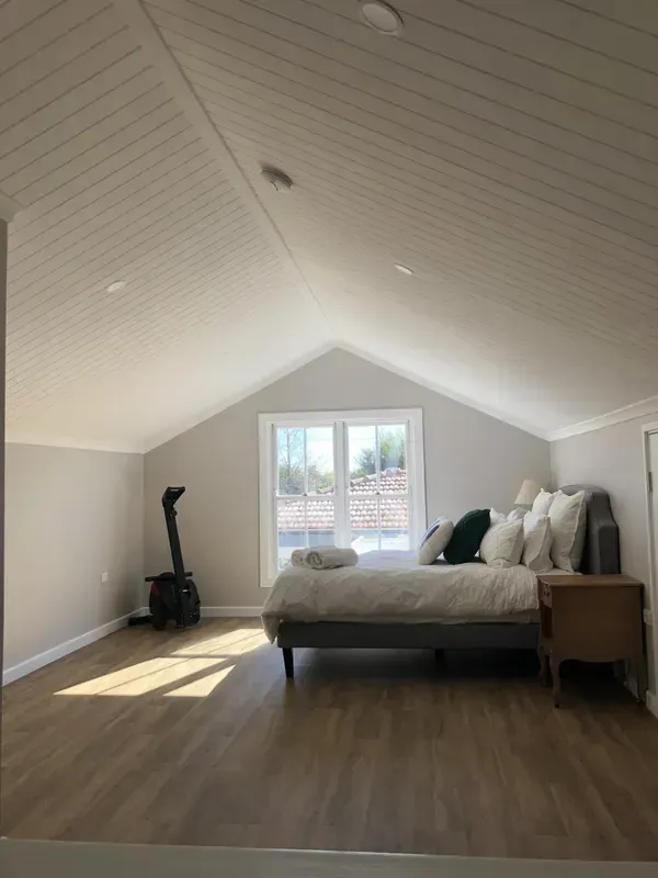Bright Attic Bedroom with Sloped White Ceiling, Bed, Nightstand, and Sunlight — Boyne Building & Renovations in Ponto, NSW