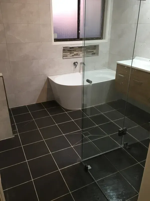 Bathroom with Black Tile Floor, White Tub, Glass Shower Screen — Boyne Building & Renovations in Ponto, NSW