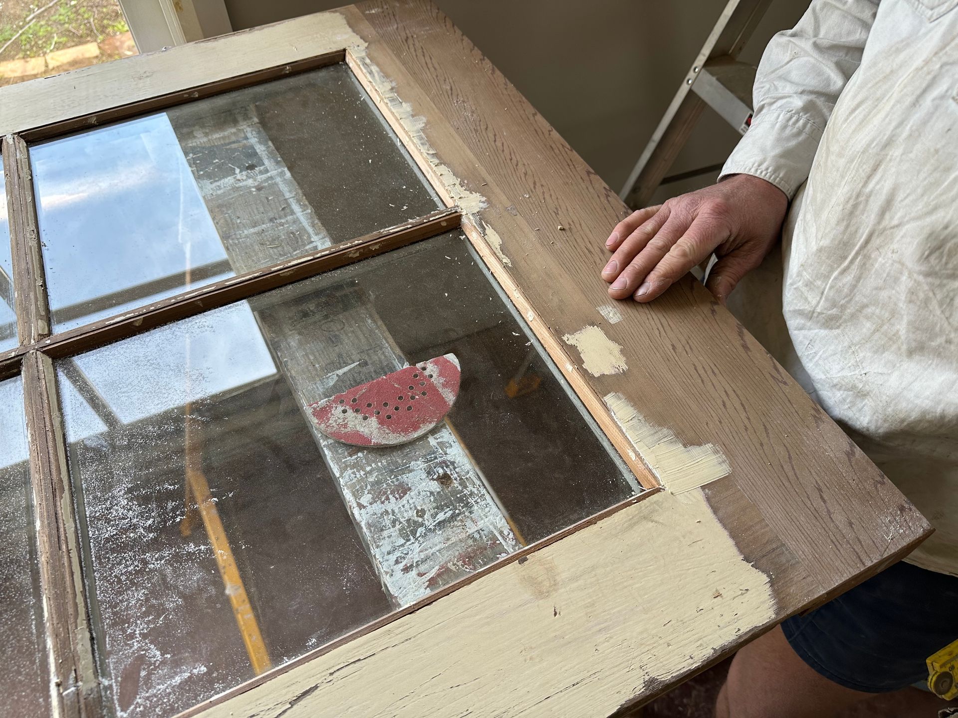 Person holding a small wooden-framed window pane with frosted glass and a red sticker.