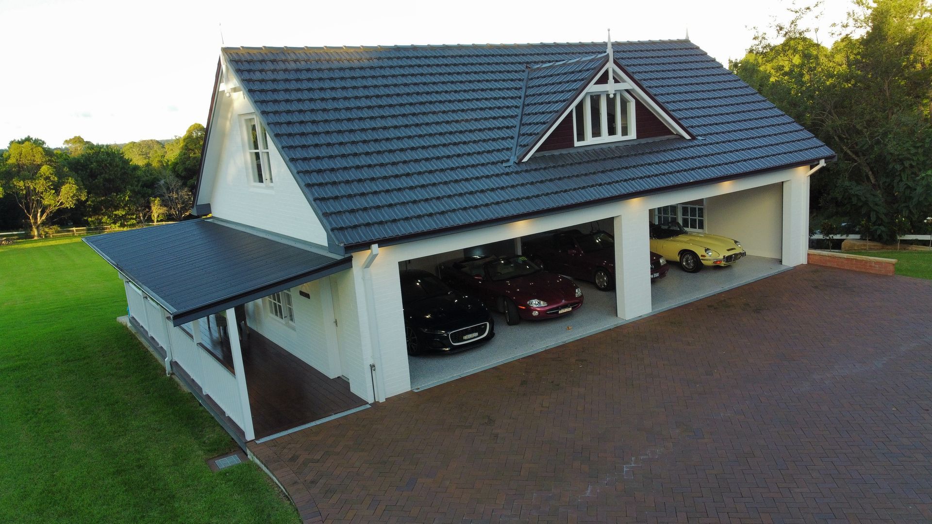 A large gray house with an open garage, parked cars, and a green lawn at sunset.