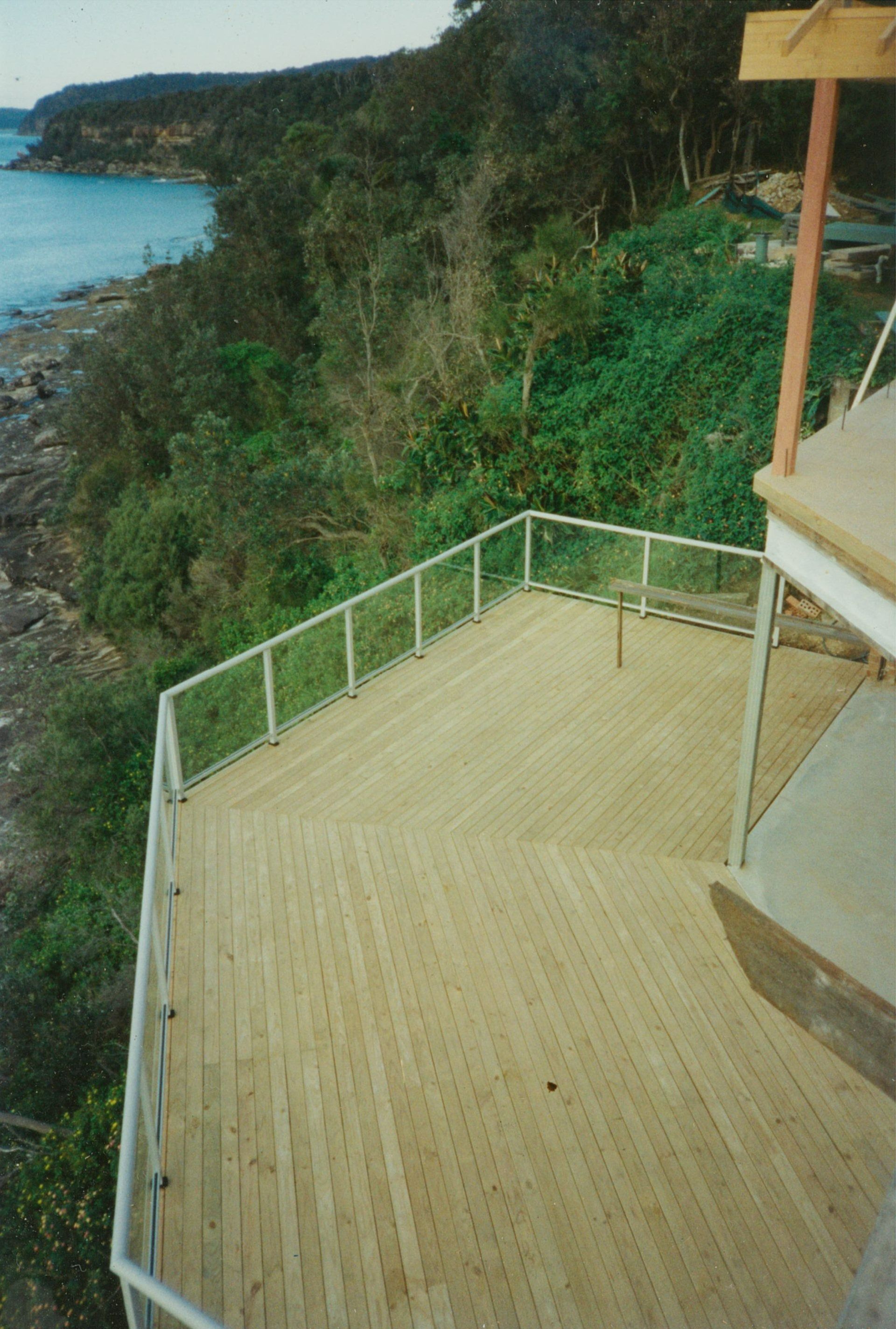 Wooden Deck with White Railing Overlooking a Rocky Coastline — Boyne Building & Renovations in Ponto, NSW
