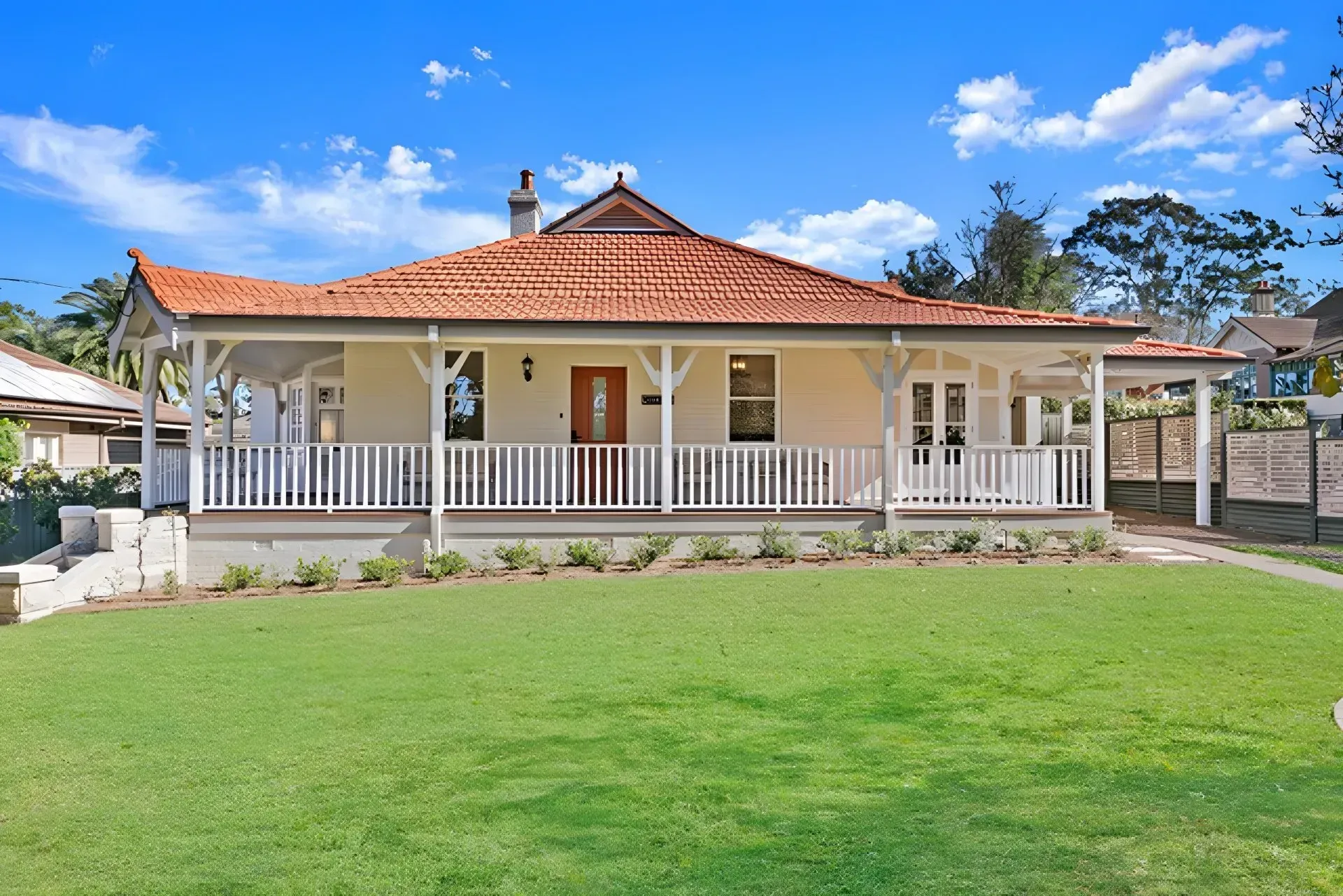 Single-story house with a red-tiled roof, white porch, and a green front lawn under a blue sky
