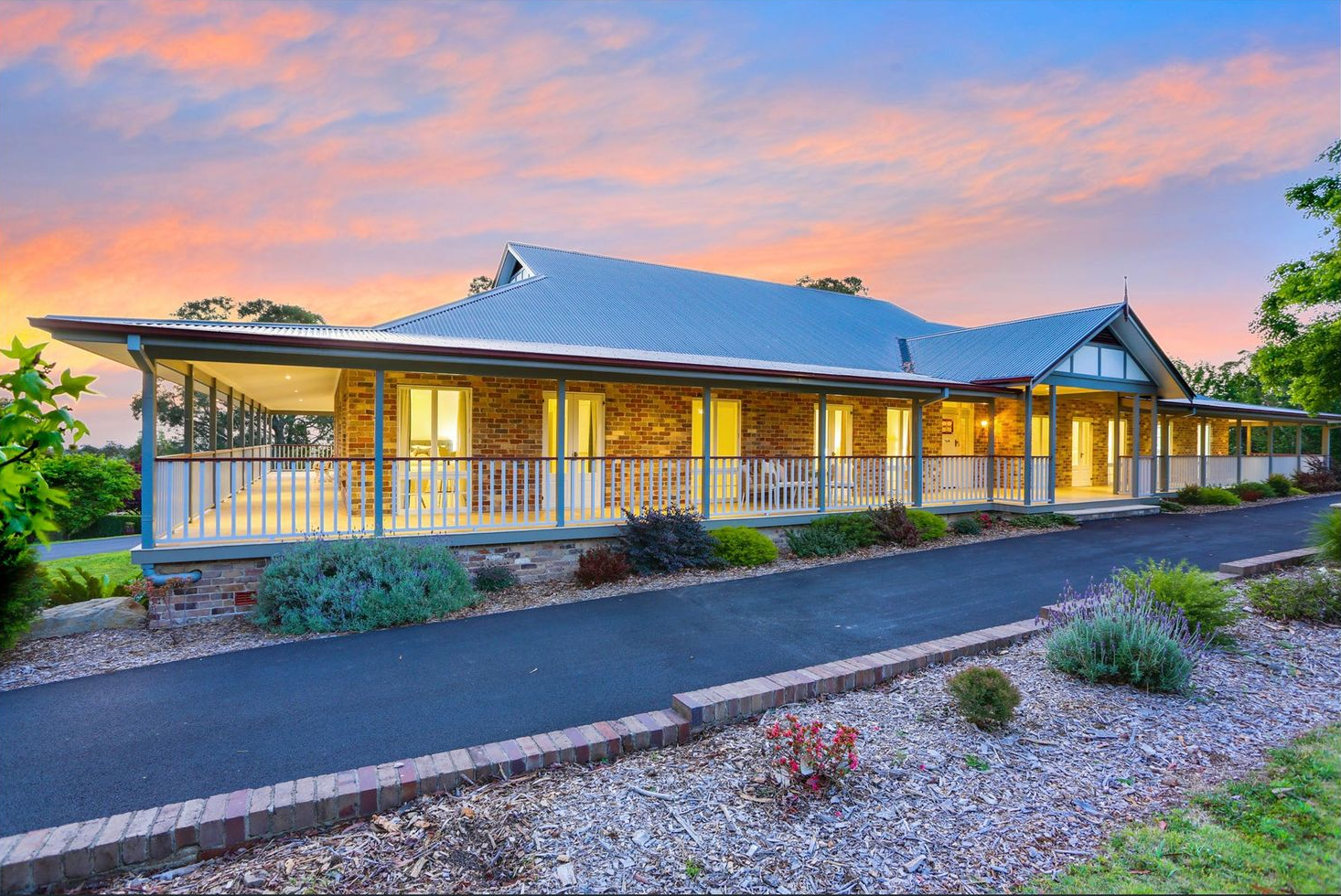 Single-story home with lit porch at sunset, framed by gravel landscaping and a colorful sky