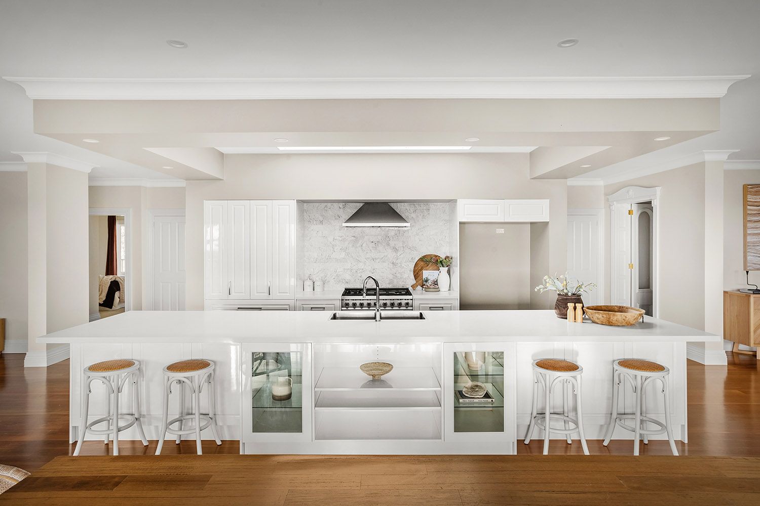 Bright white open kitchen with central island, bar stools, and large windows in a modern home