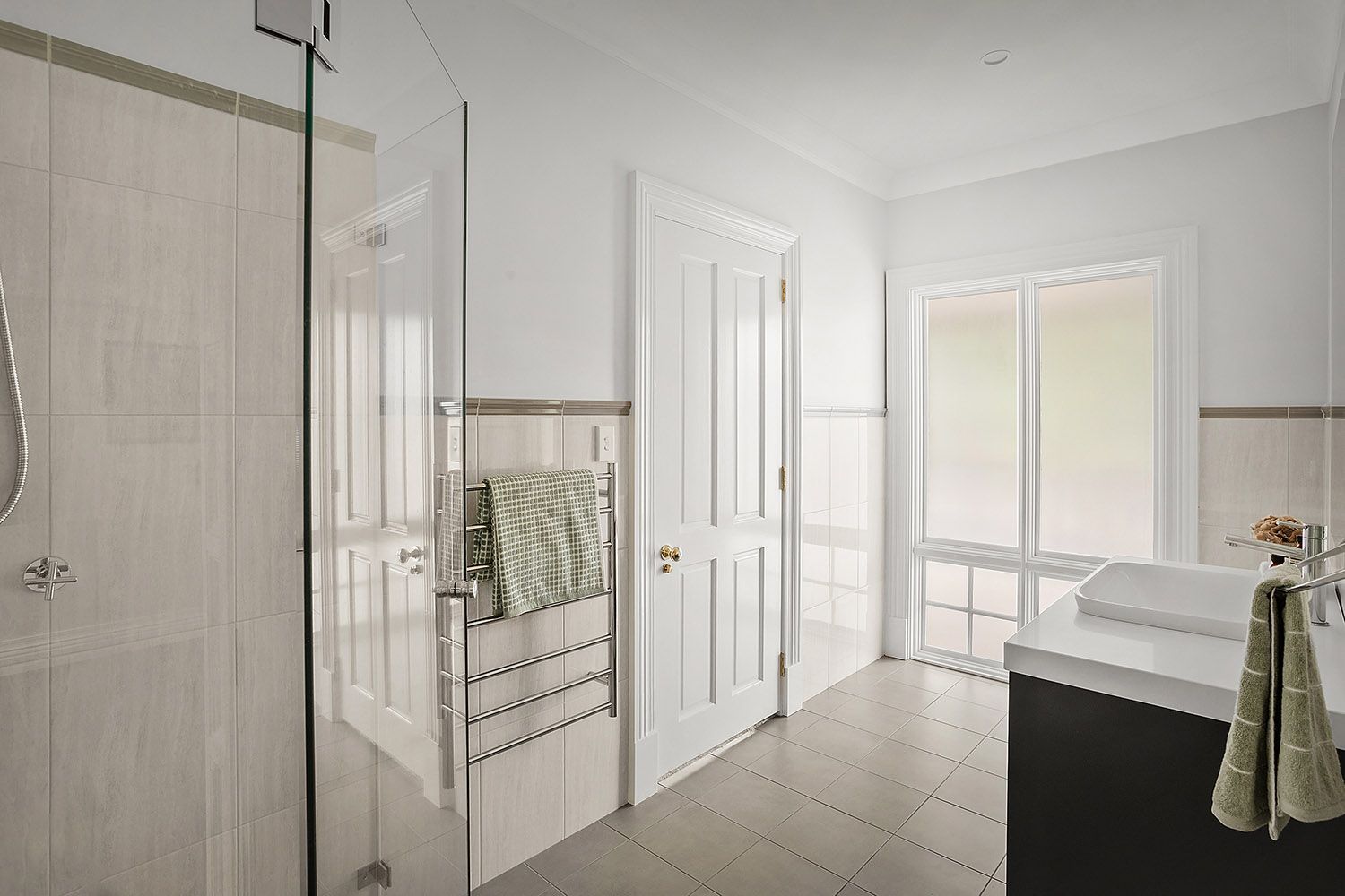 Bright white bathroom with glass shower, vanity, towel rack, and sliding doors to a balcony.