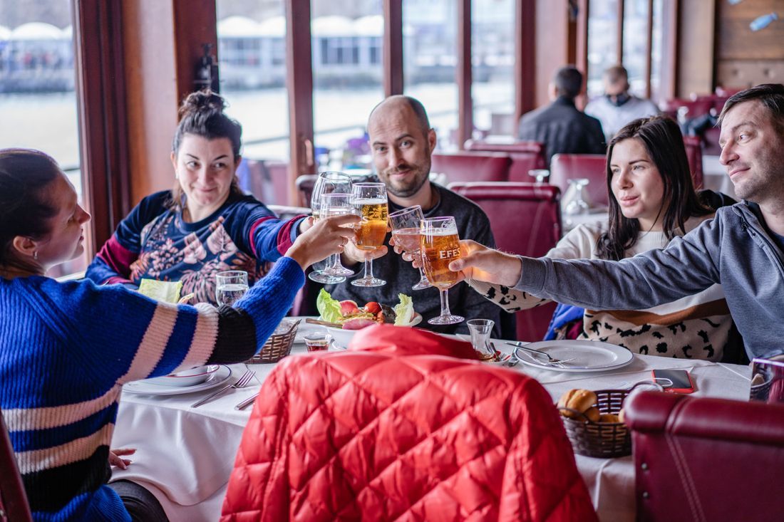 Friends clinking beer glasses at a restaurant table with a red jacket draped over a chair