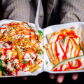 Two takeout dessert trays drizzled with red, white, and green sauce, held in front of a person