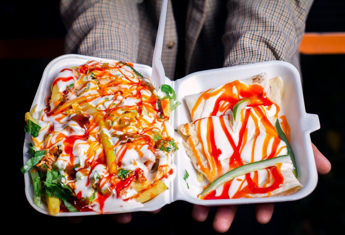 Two foam takeout boxes with sauced food, held in someone's hands against a dark background