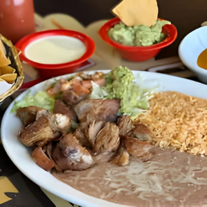Plate of Mexican food with rice, refried beans, grilled meat, tortilla chips, and salsa on the side