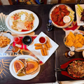 Overhead view of a table with tacos, burgers, fries, nachos, wings, and drinks